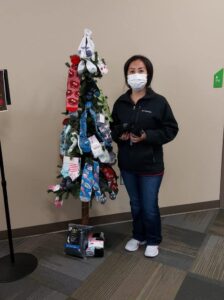 Student Mina Vang-Xiong volunteers for the spring sock collection. She is standing next to a Christmas tree covered in socks.