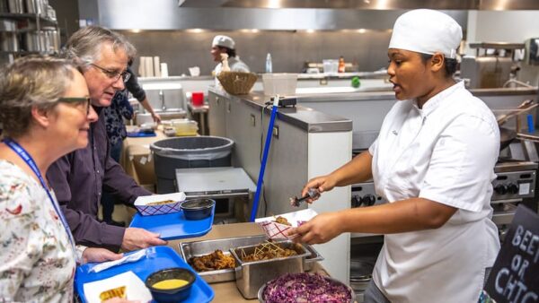 Culinary student serving food to two women.