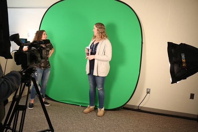 Another marketing student standing in front of green screen and being recorded by a professional video camera.