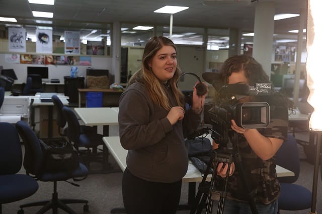 Marketing student standing behind a professional camera.