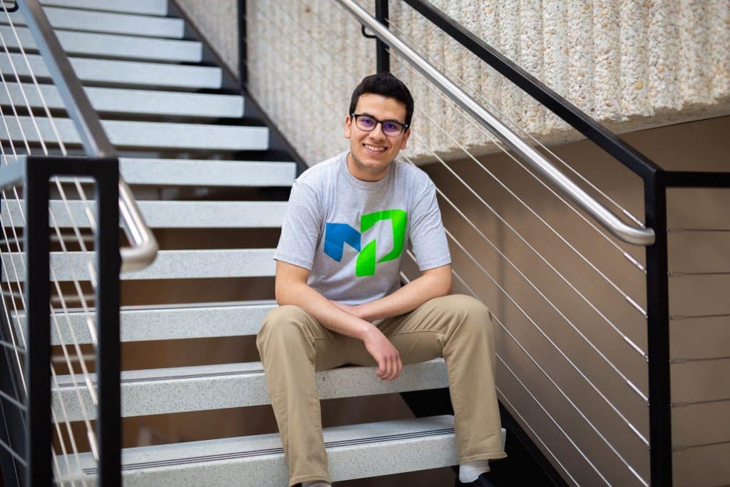 Male student sitting on stairs smiling at the camera.