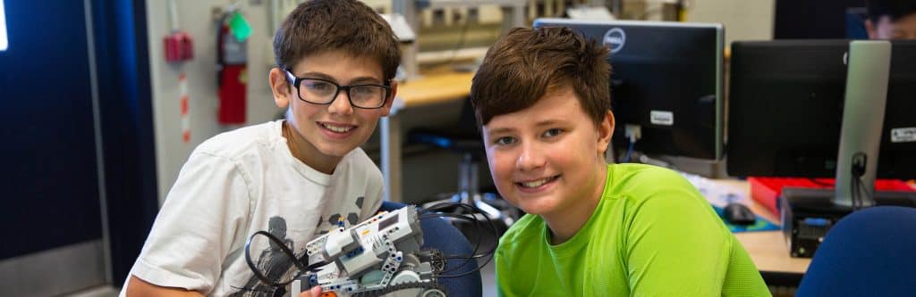 Two smiling middle school students playing with a robotics arm.