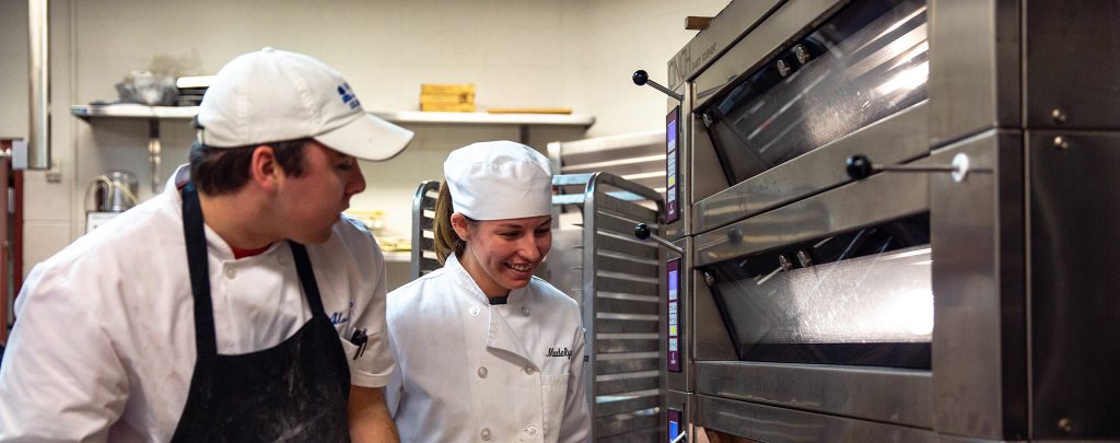 two culinary students standing near oven
