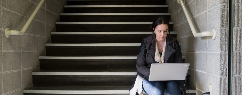 female student sitting on stairs holding laptop