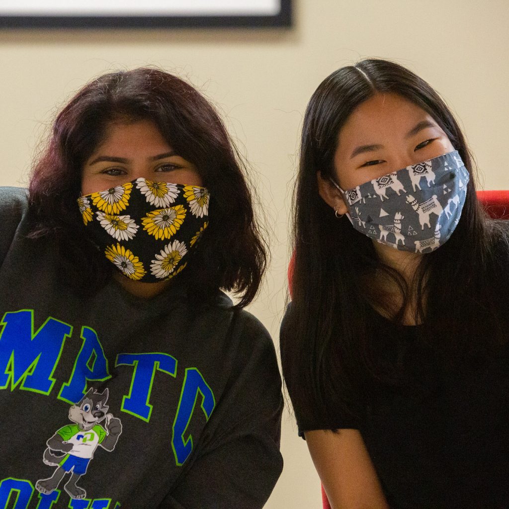 two female students smiling at the camera wearing masks