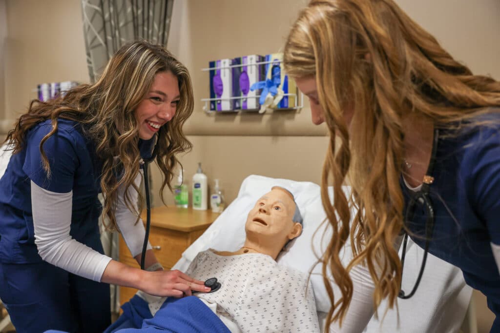 Two nursing students listening to the heartbeat of a patient dummy.