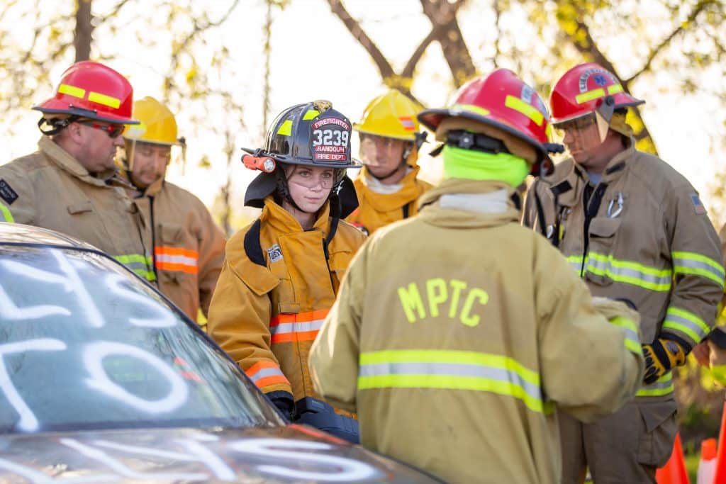 Moraine Park Fire Protection Program Students in firefighter uniform standing next to a car.