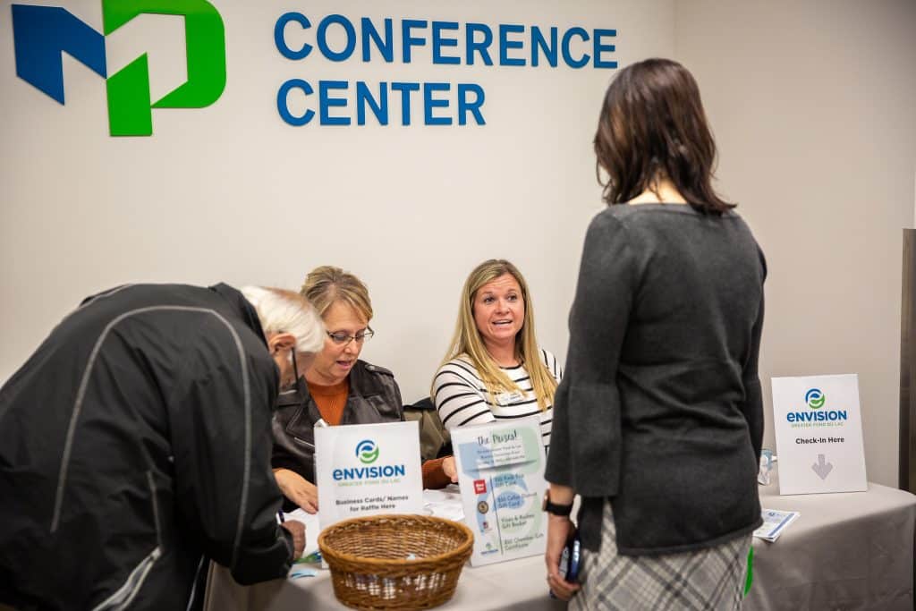 Two people sitting at a table and checking in two standing people to the Moraine Park Conference Center.