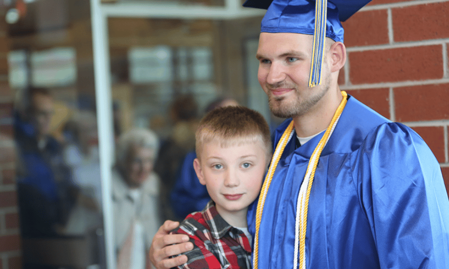 Graduate in cap and gown next to younger brother. Both are smiling.