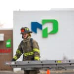 A fire fighter carrying a ladder in front of building with the Moraine Park Logo