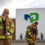 Two fire fighters dressing up in front of building with a large Moraine Park logo.