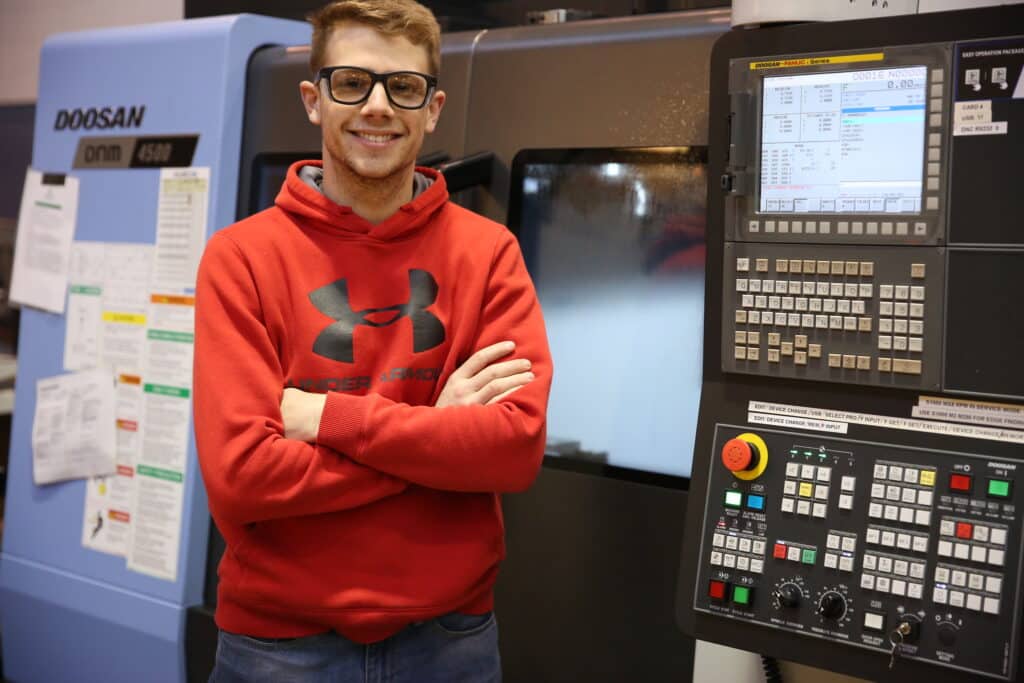 Smiling student standing in front of CNC machine.