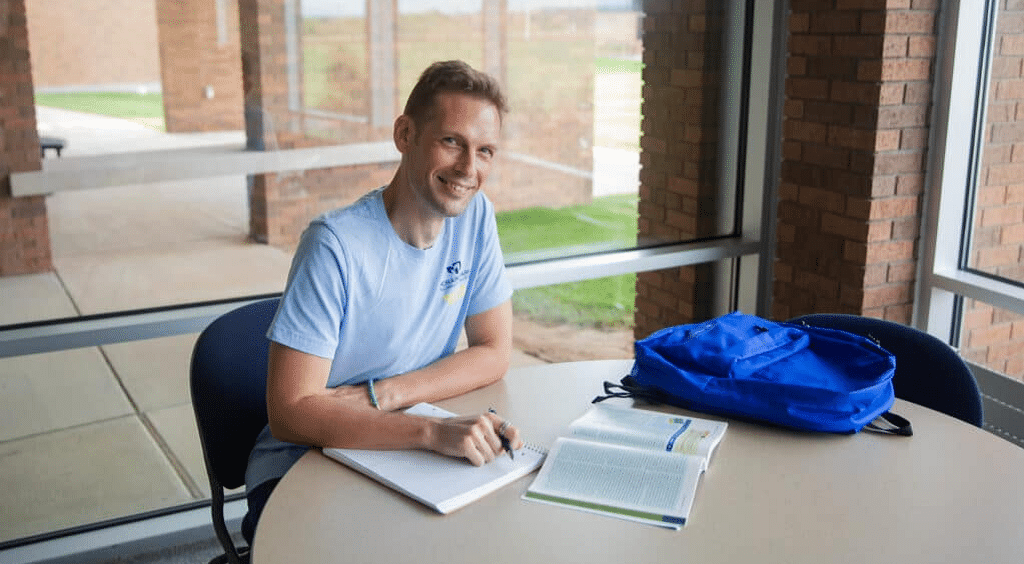 Image of veteran student, Donald Shobo, doing homework at a desk and smiling into the camera.