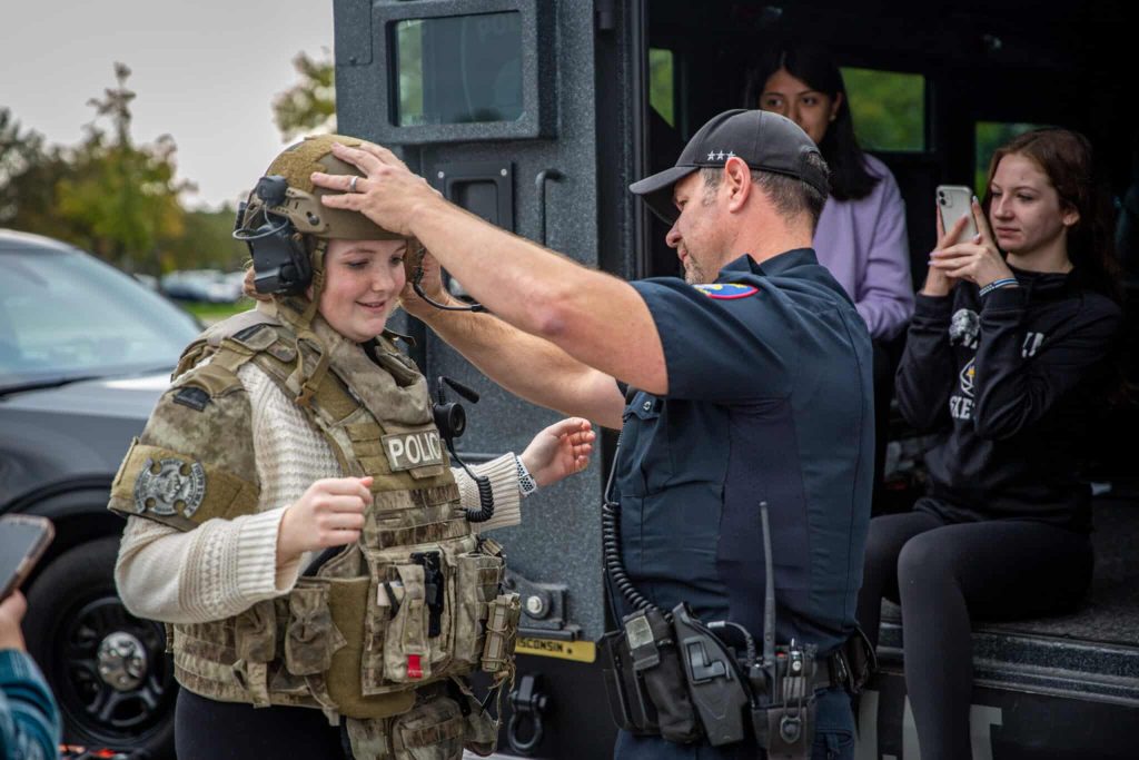 Police man dressing a student in protective gear as demonstration for other students.