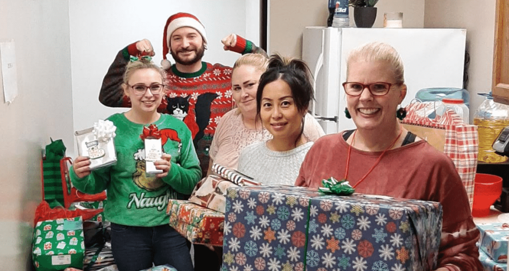 Four Moraine Park volunteers dressed in Christmas sweater holding gifts.