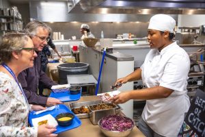 Culinary student serving food to two women.
