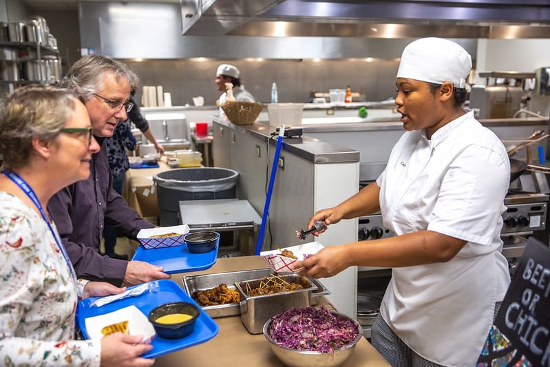 Culinary student serving food to two women.