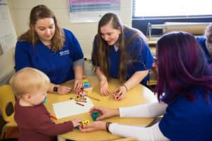 Early Childhood Education students in a classroom setting with a toddler —playing games and learning.