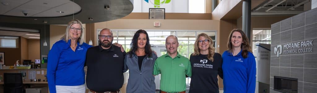 The happy Moraine Park recruitment team standing next to each other in the Fond du Lac Campus lobby.