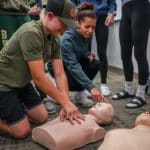 Two students are practicing CPR on a dummy.