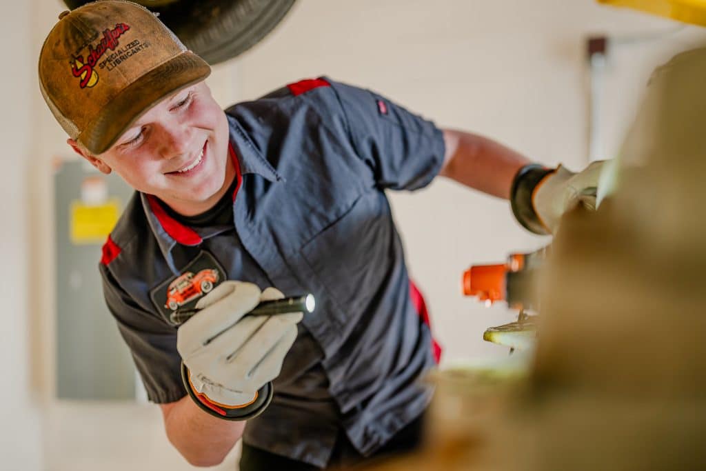 Smiling male Moraine Park automotive student shining light onto a car engine.