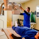 Radiography student adjusting a machine with the patient waiting.