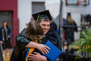 Moraine Park student in graduation gown hugging another student with the degree in their hand.