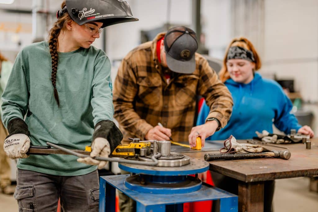 Three manufacturing students bending a piece of metal.