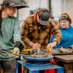 Three manufacturing students bending a piece of metal.