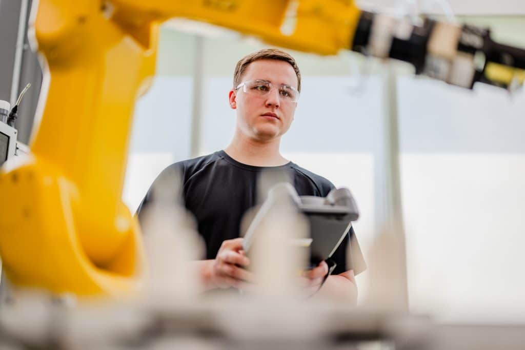Manufacturing student operating a yellow robot arm.