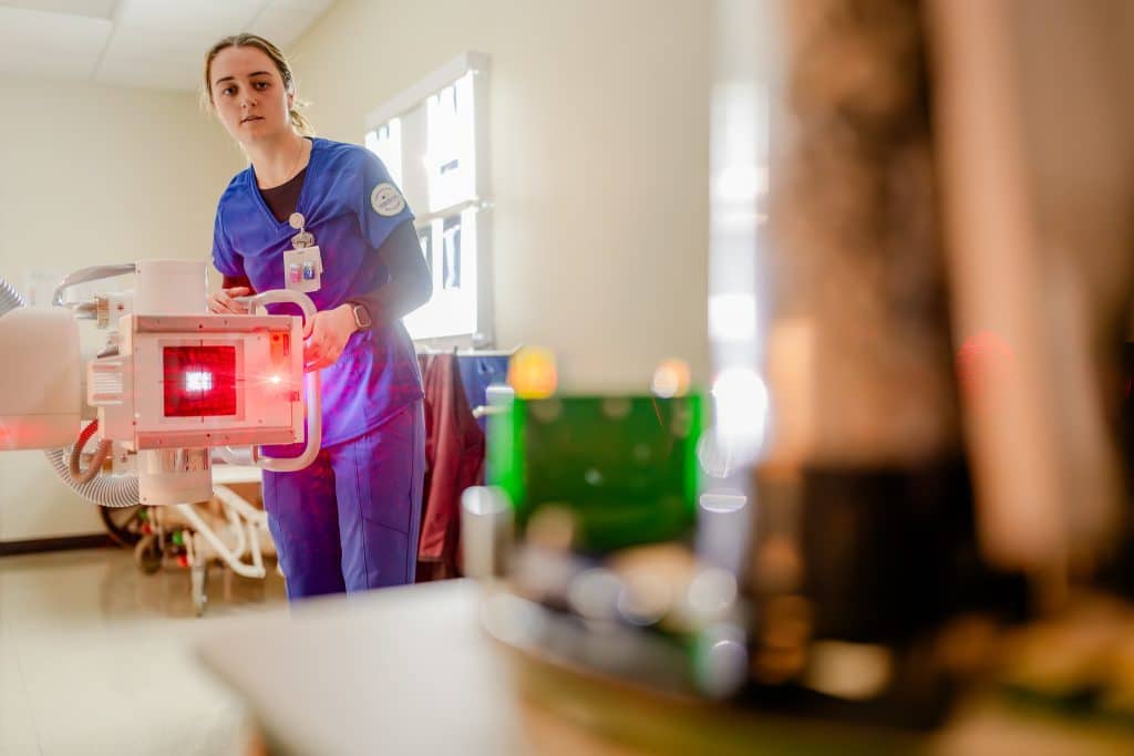 Radiography student adjusting a machine that radiates red light.