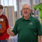 Moraine Park robotics instructor introducing a green robotic arm in front of high school students.