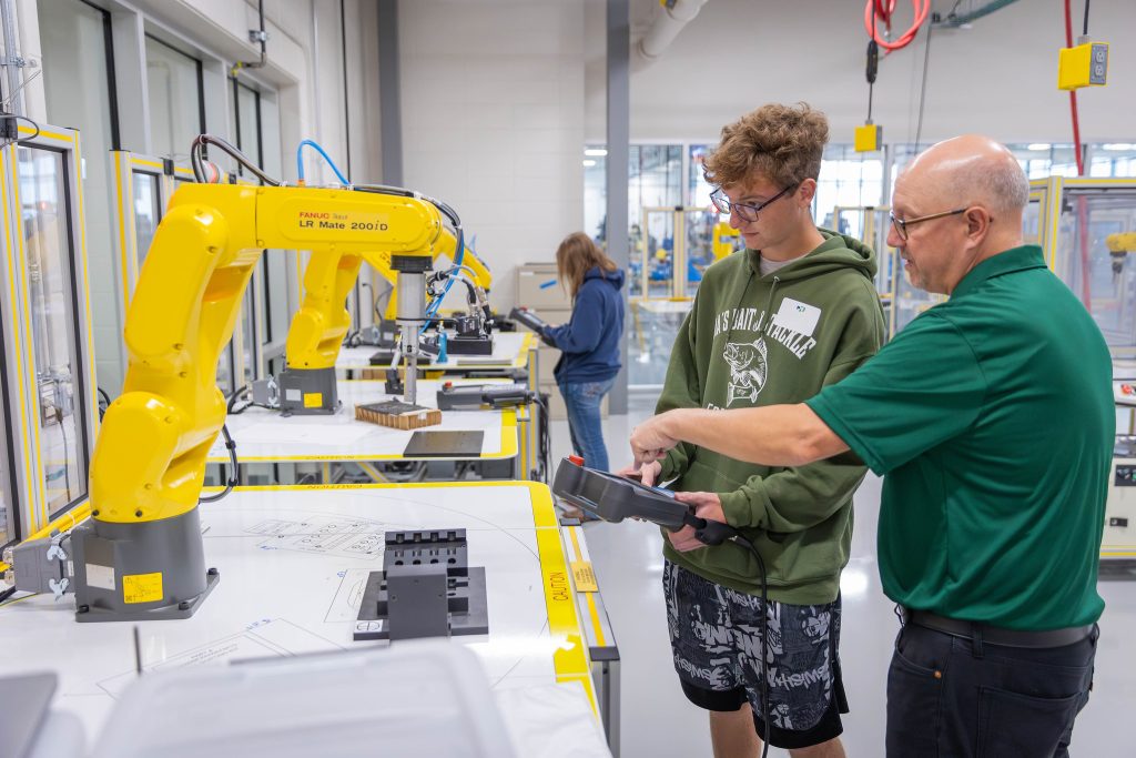 High school student controlling a yellow robotic arm with a remote control.