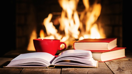 Books laying on a table with a read cup. There is a fire in the background.