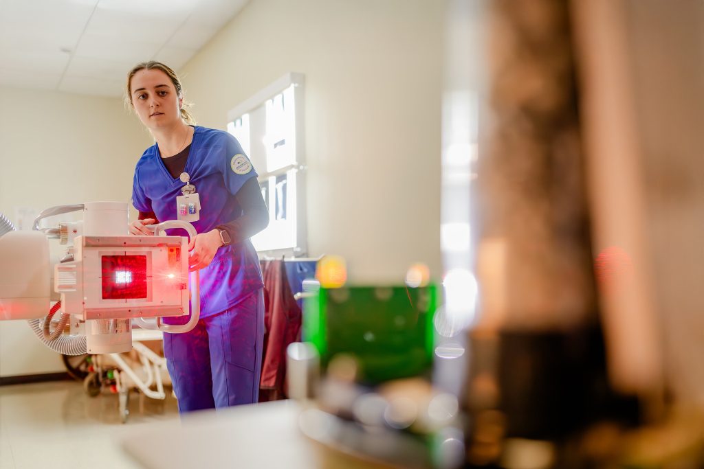 Radiography student adjusting a machine that radiates red light.