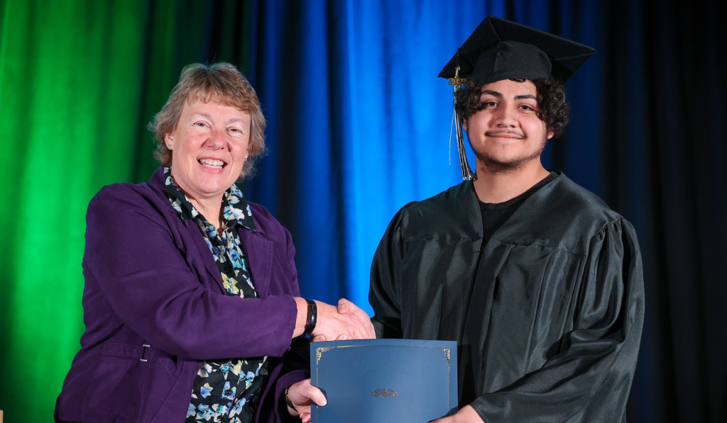 Bonnie Baerwald and Journey program student shaking hands and smiling on the stage at graduation.