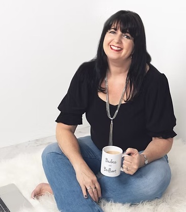 Smiling Wendy Wilson Burich sitting on a comfortable white carpet and holding a cup of hot coffee.
