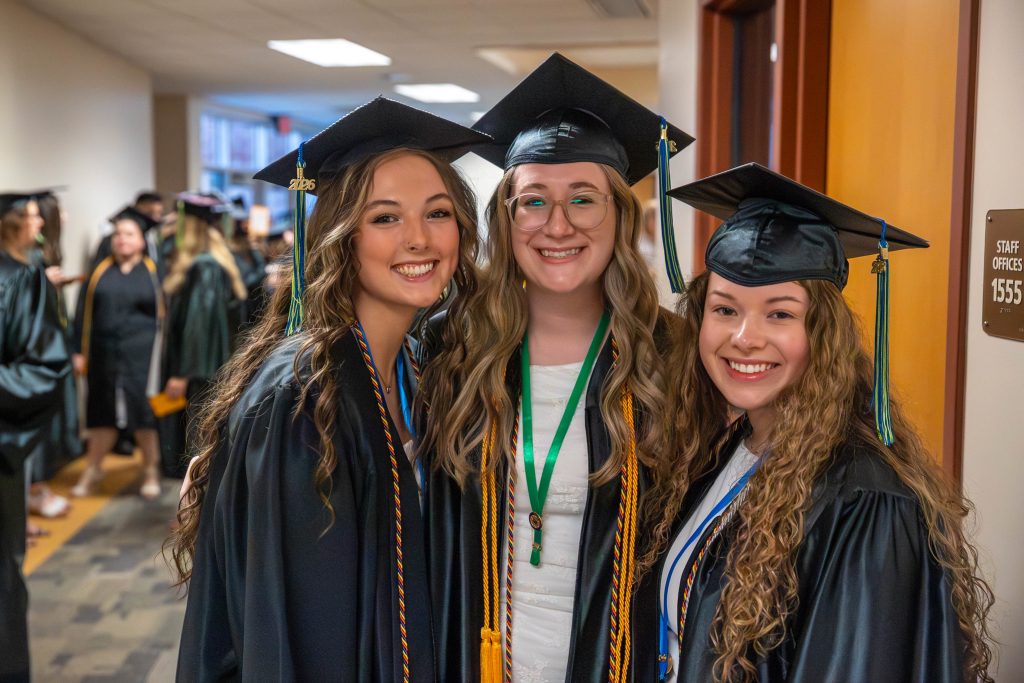 Three graduates posing together and smiling.