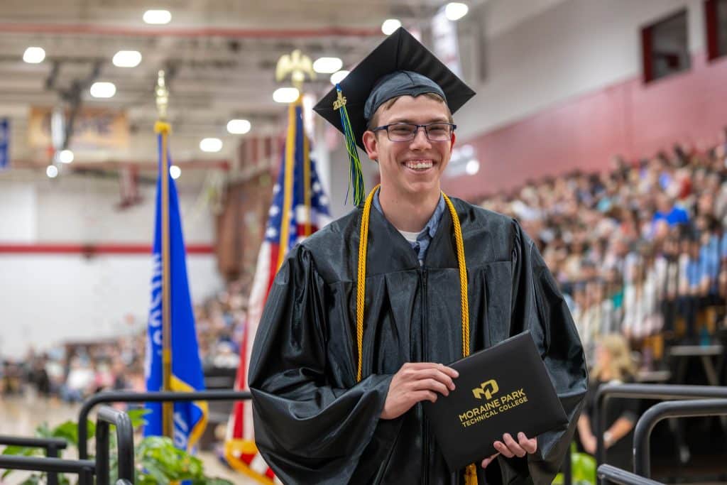 Male student smiling on stage at spring 2026 commencement ceremony.