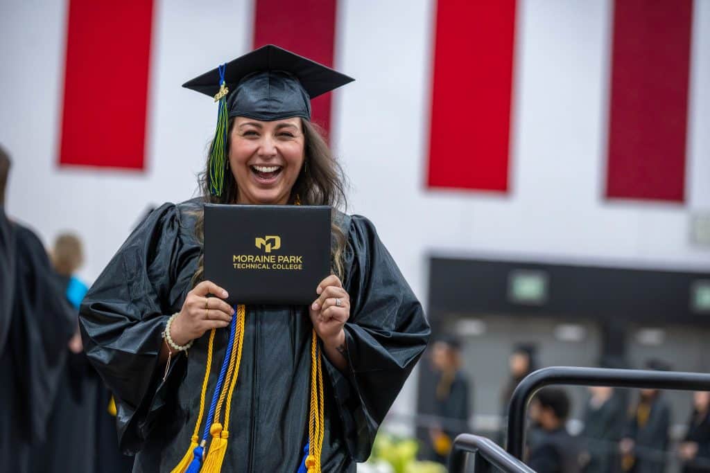 Student in regalia at commencement smiling with her diploma cover.